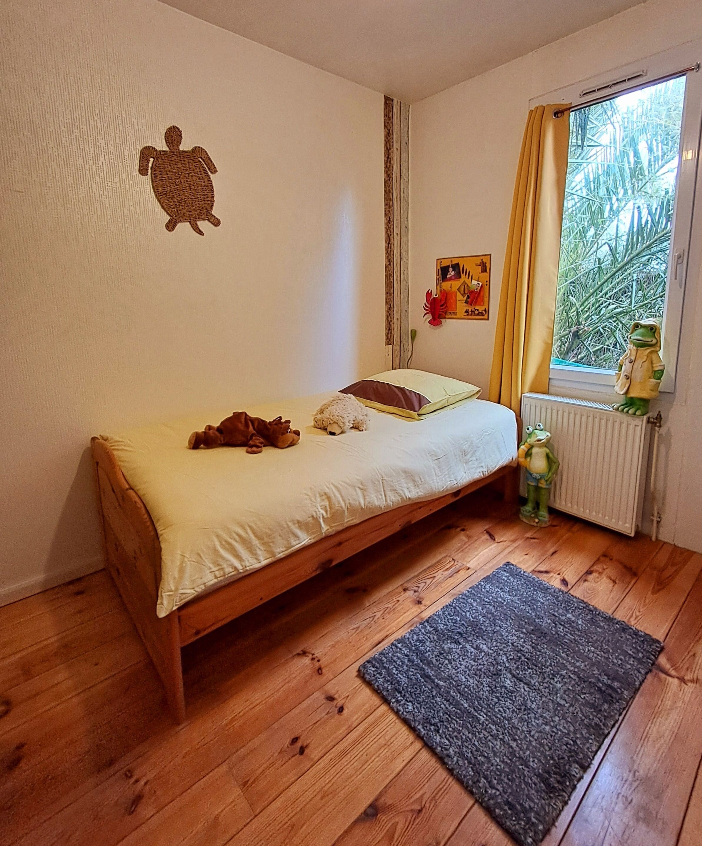A small, cozy bedroom with a single bed, a wooden floor, a radiator, and a window with curtains.