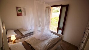 Quarto com duas camas, abajur, janela com vista e uma obra de arte na parede.