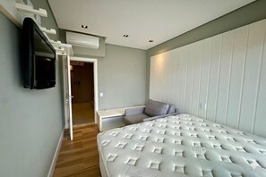Ein Schlafzimmer mit Bett, Wandfernseher, integriertem Sitzplatz und einer Tür zu einem anderen Raum.
