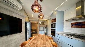 A modern kitchen with a wooden dining table, built-in appliances, and pendant lighting. - Luxury Garden in Riviera: Where the Garden Meets the Beach (Bertioga)