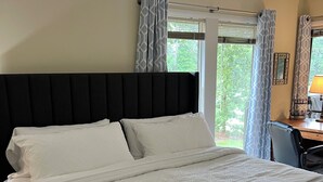 Un dormitorio con una cama grande, cabecera, escritorio con silla y ventana con cortinas.