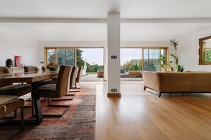 A spacious living area with a dining table, sofas, and a large window offering a view of the outdoors. - Ty Castel Guest Room 2 with Pool, Terrace and Wi-Fi (Ploeren)