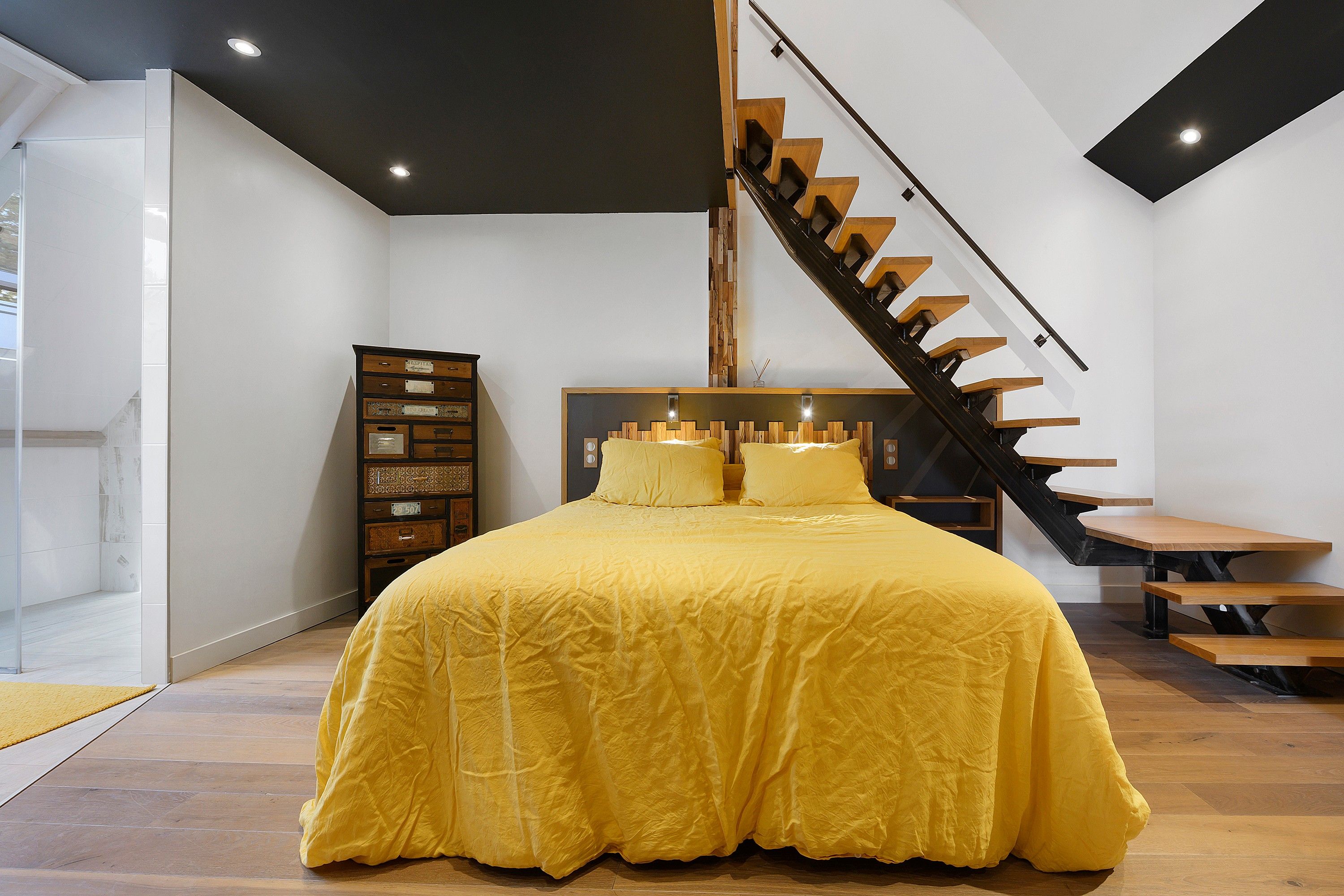 Quarto com uma cama grande, penteadeira de madeira e escada.