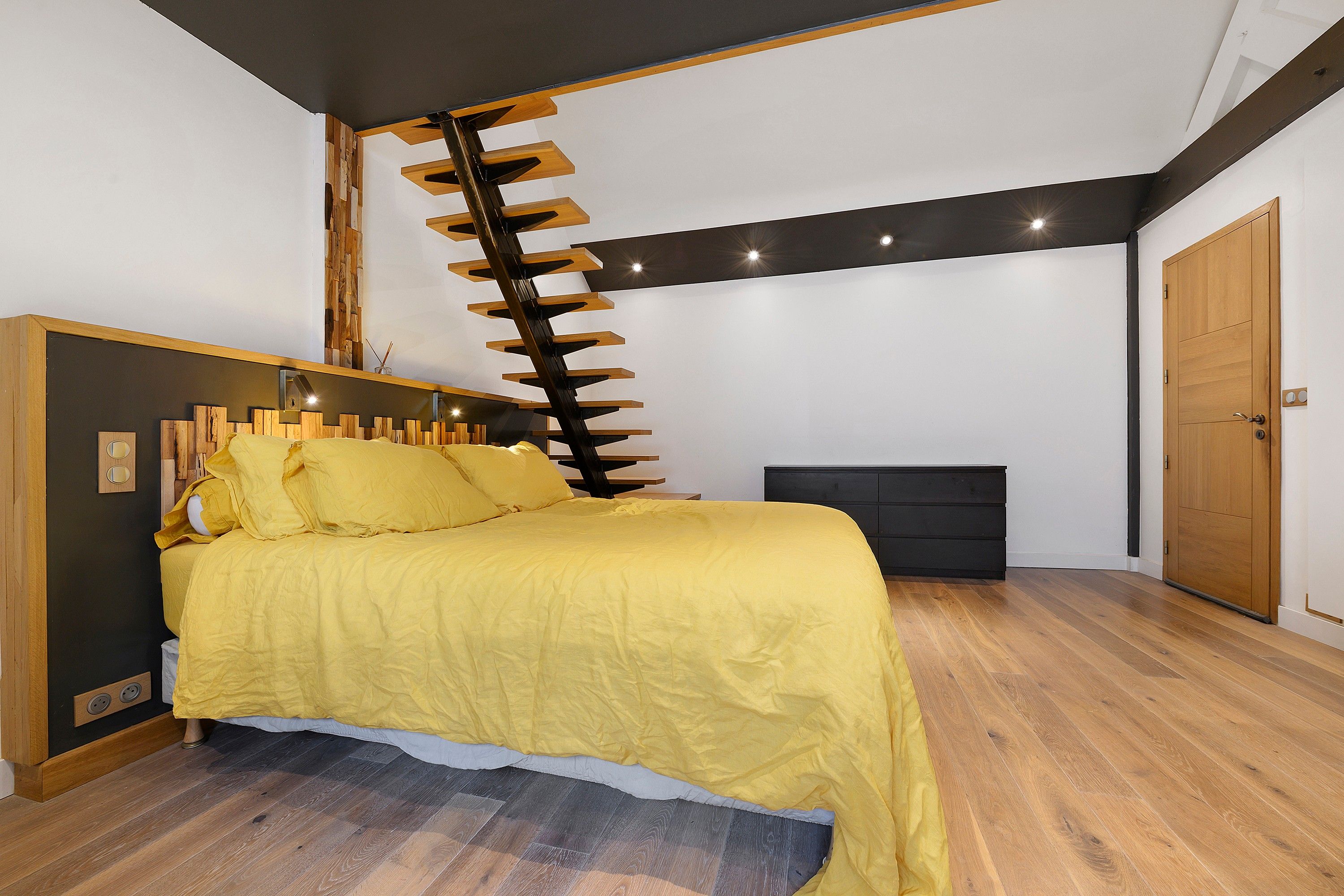 Een slaapkamer met een bed, een houten trap, een dressoir en een deur.