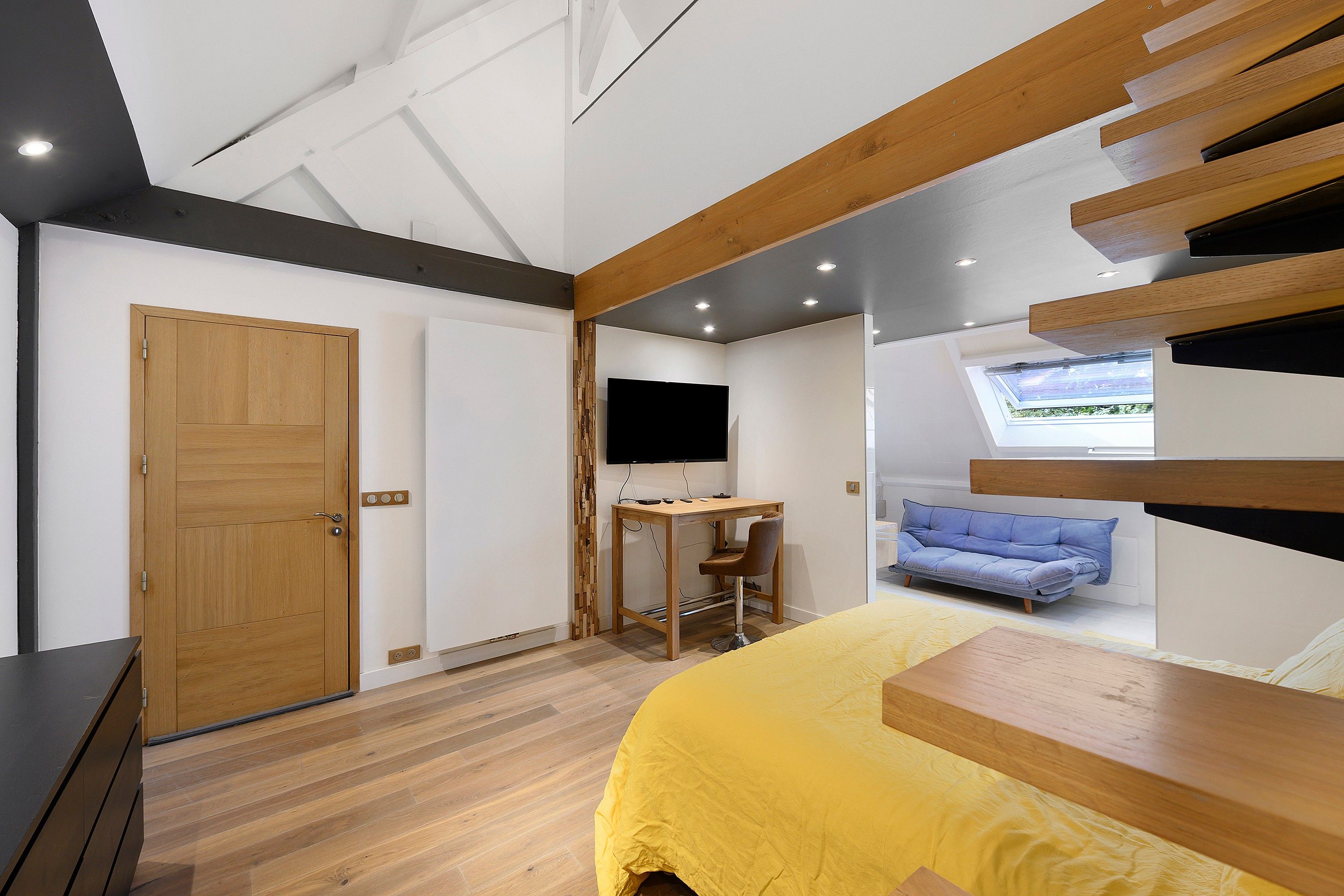 A bedroom with a bed, a desk, a chair, a television, and a window.