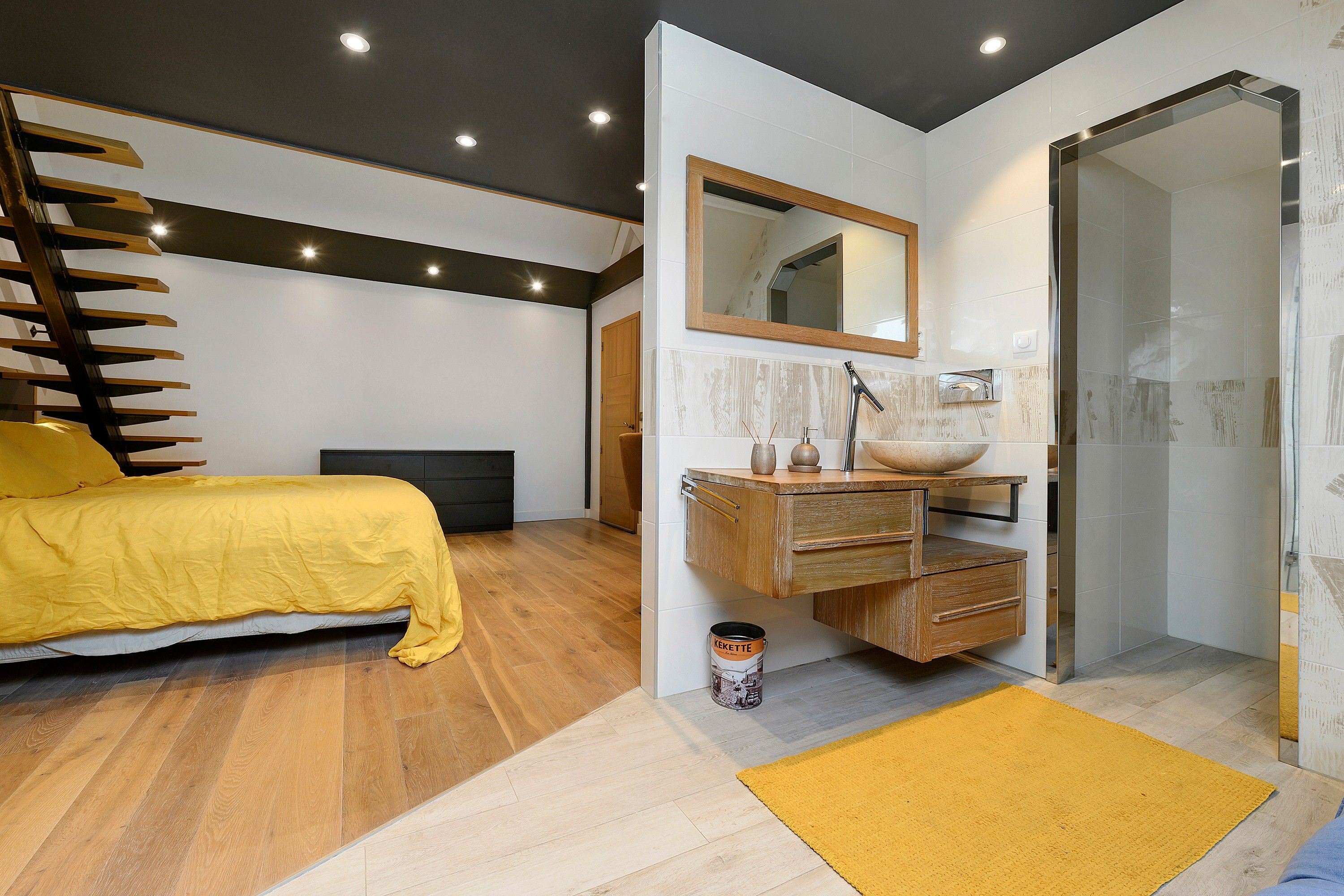 Un dormitorio moderno con cama, cómoda de madera, espejo y zona de ducha.