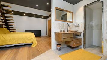 Un dormitorio moderno con cama, cómoda de madera, espejo y zona de ducha.