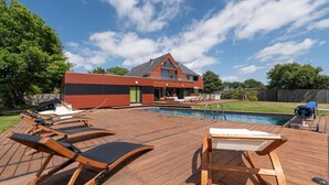 Une maison moderne dotée d’une piscine, d’une terrasse en bois et de chaises longues.