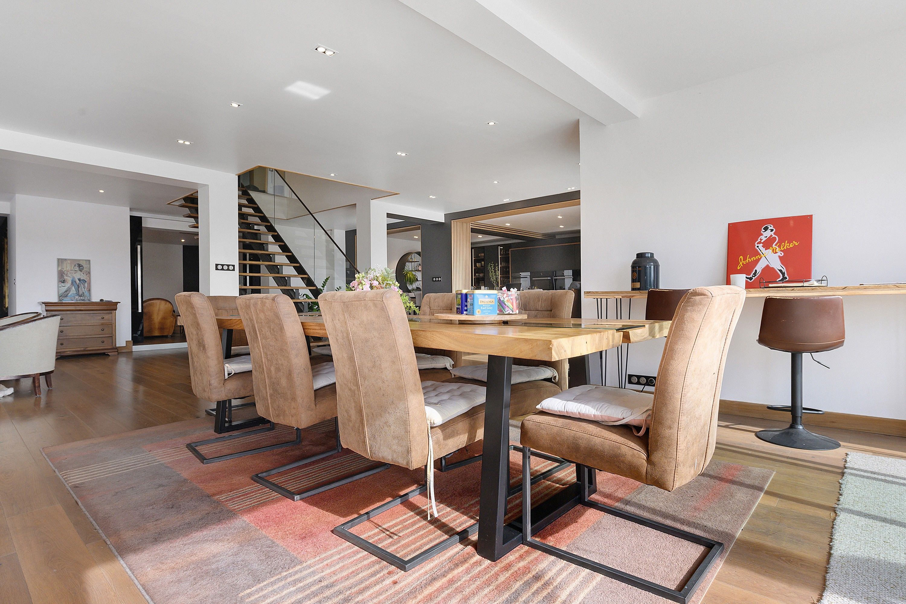 Ein moderner Essbereich mit einem Holztisch, gepolsterten Stühlen, einer Treppe und einer Küche im Hintergrund.