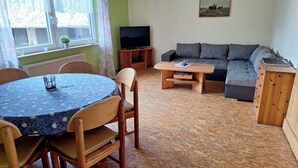 A living room with a round wooden table, a sofa, and a television. - Cozy vacation apartment at the Hainerhof (Grünberg)