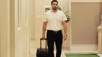 A man walking down a hallway with a suitcase, a sign indicating an exit, and a wall-mounted device.