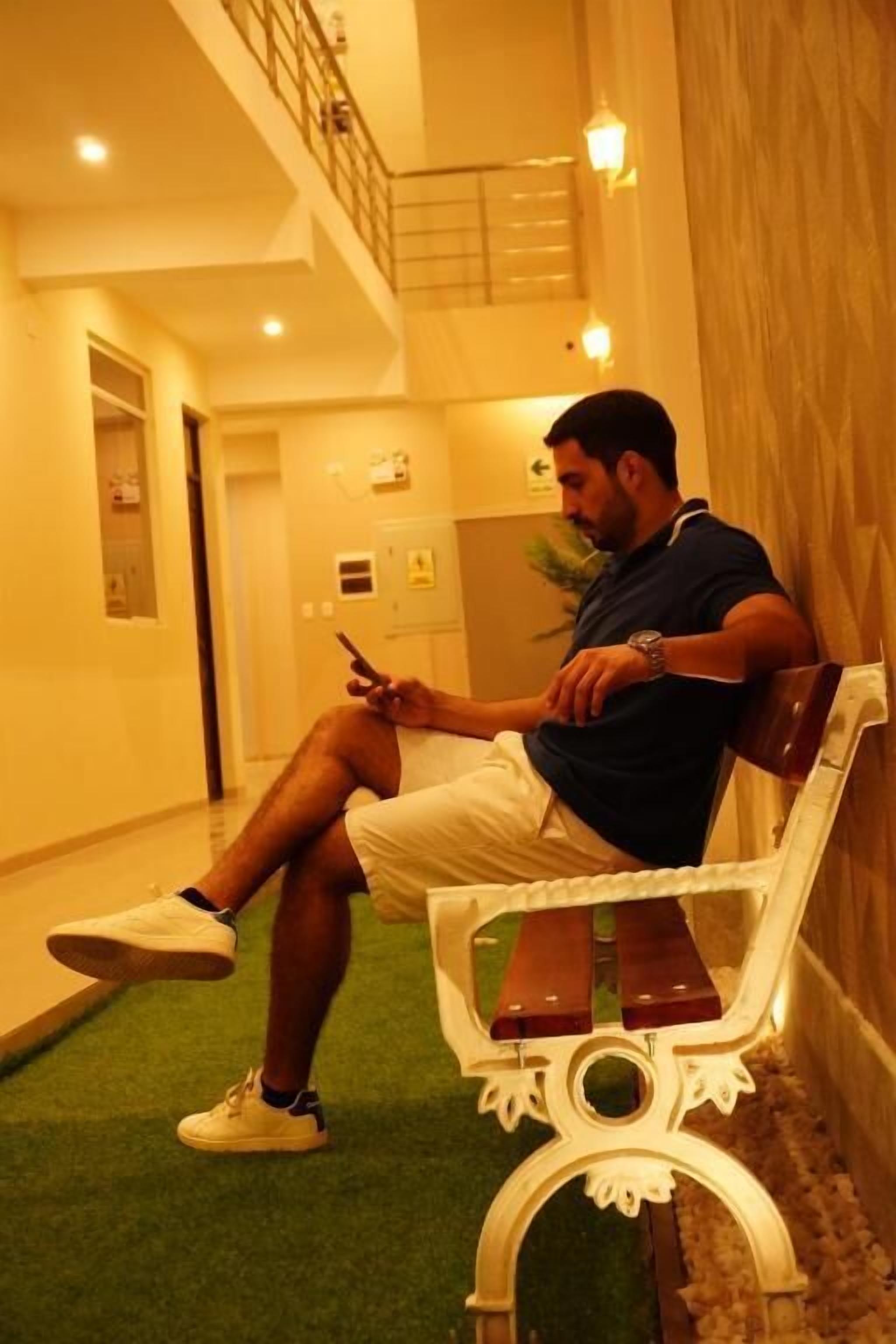 A man sitting on a bench in a hallway with a staircase in the background.