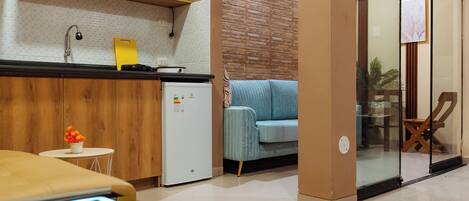Cocina moderna con microondas, lavamanos y un refrigerador pequeño. Hay un sofá azul y una puerta de vidrio que da a un balcón.