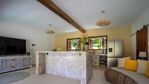 A modern kitchen with a central island, a dining area with a sofa, and a TV in the living room. - Casa Limone (Porto Seguro)