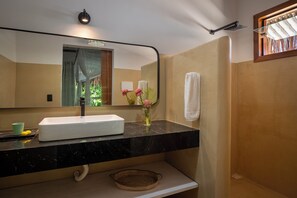 Une salle de bain avec un lavabo blanc, un plan de toilette noir et un miroir au-dessus.