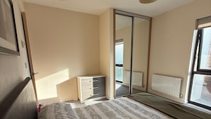 Ein Schlafzimmer mit Bett, Kommode, Spiegel und Fenster.