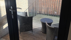 Ein Balkon mit Korbmöbeln, einem Metallgeländer und einer Ziegelwand im Hintergrund.