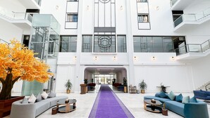 Un hall espacioso con una alfombra púrpura en el centro, mobiliario moderno y un gran árbol con hojas otoñales.