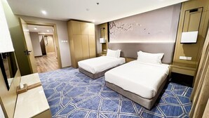 Habitación de hotel con dos camas, un espejo grande, televisor montado en la pared y una alfombra con estampado geométrico.