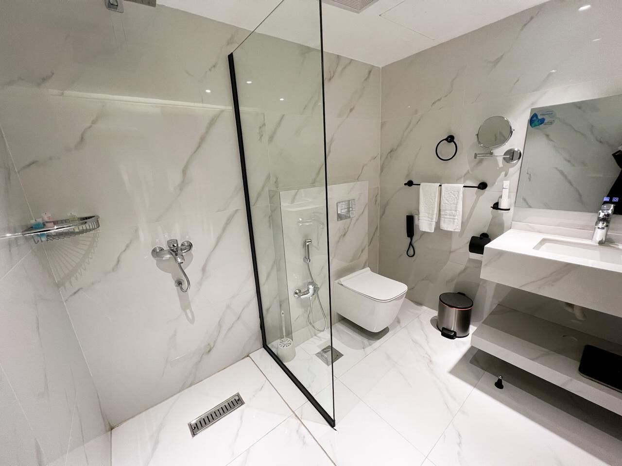 Un baño moderno con ducha de vidrio, inodoro y tocador con lavamanos.