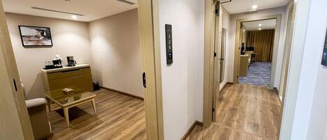 A hotel hallway with wooden flooring, a glass table, a beige sofa, and a small cabinet.