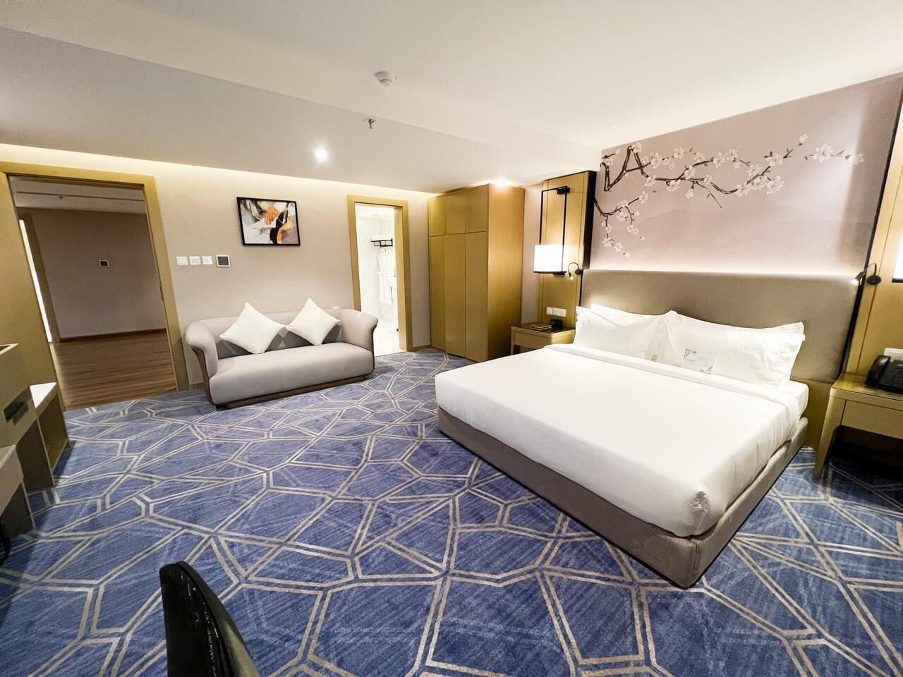 A hotel room with a large bed, a sofa, a desk, and a mirror.