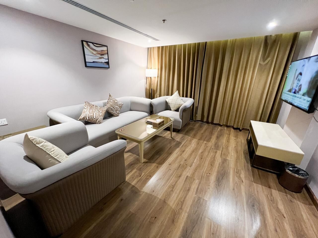 A modern living room with a sectional sofa, a coffee table, a TV mounted on the wall, and a window with curtains.