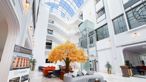 Un vestíbulo espacioso con una zona de estar central, un amplio atrium de vidrio y una escalera moderna.