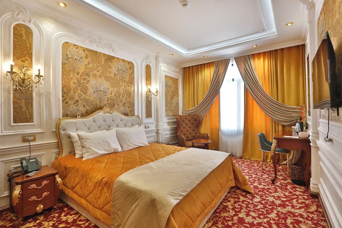 Una lujosa habitación de hotel con una cama grande, decoraciones ornamentales en la pared, un candelabro y un sillón clásico.