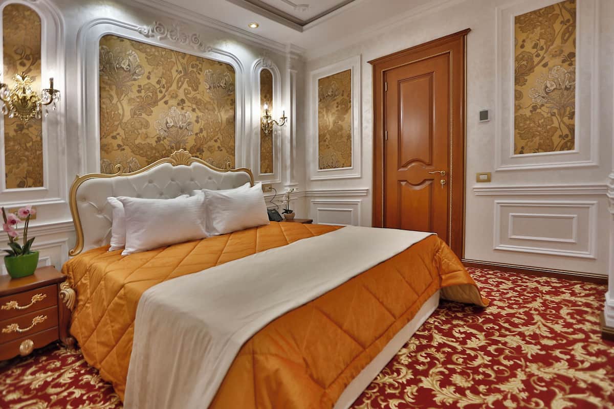 Una cama grande con cubrecama dorado y blanco, una puerta de madera y un papel tapiz decorado.