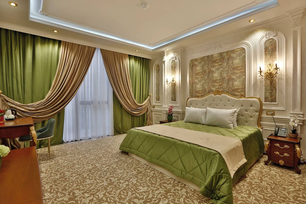 Una habitación de hotel con una cama grande, cortinas verdes, un candelabro y una alfombra estampada.