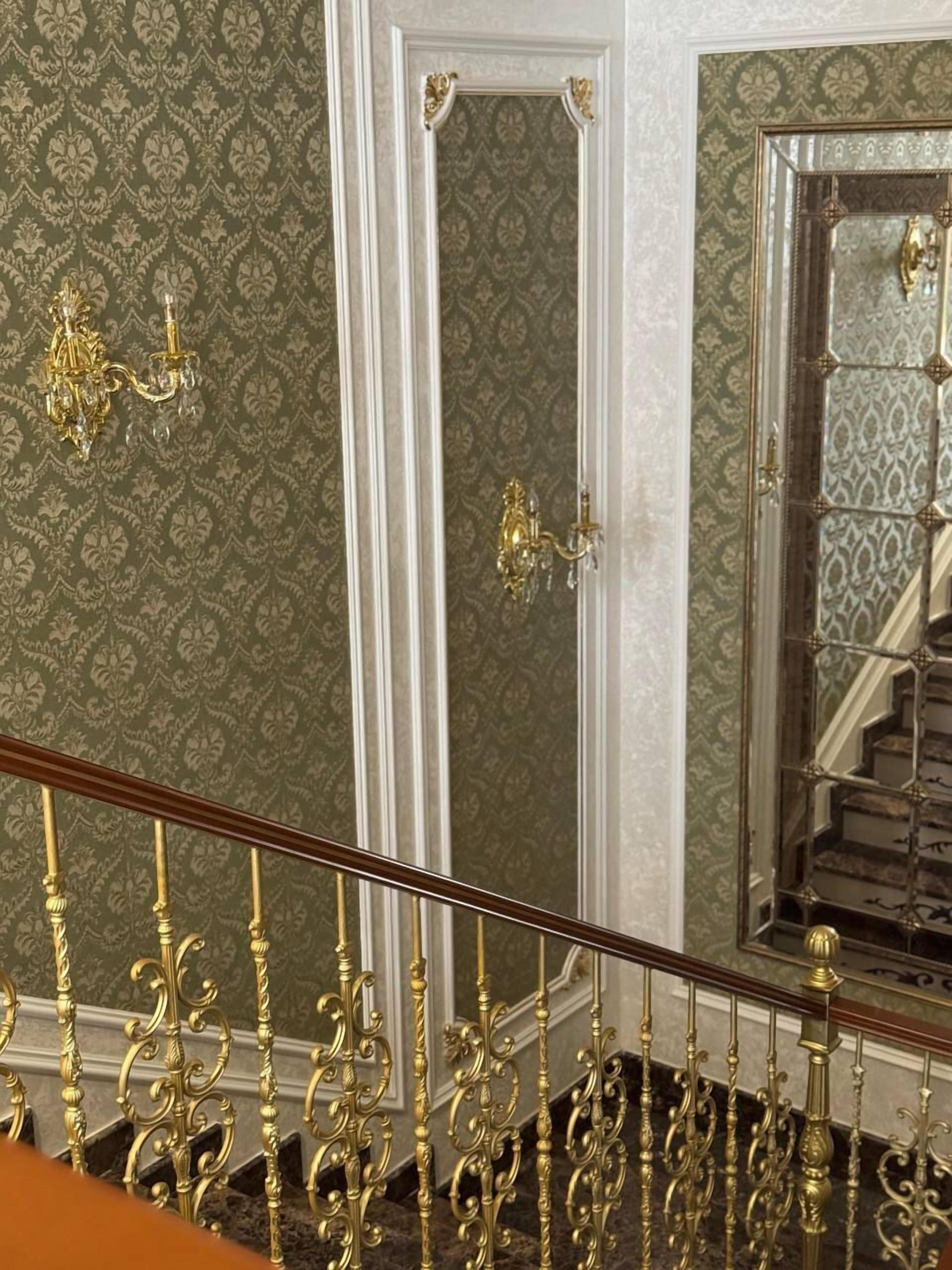 Una gran escalera con barandillas doradas ornamentadas y un espejo que refleja la escalera.
