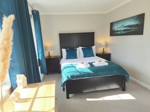 Un dormitorio ordenado con una cama, lámparas de noche, una mesita, un jarrón decorativo y un cuadro en la pared.