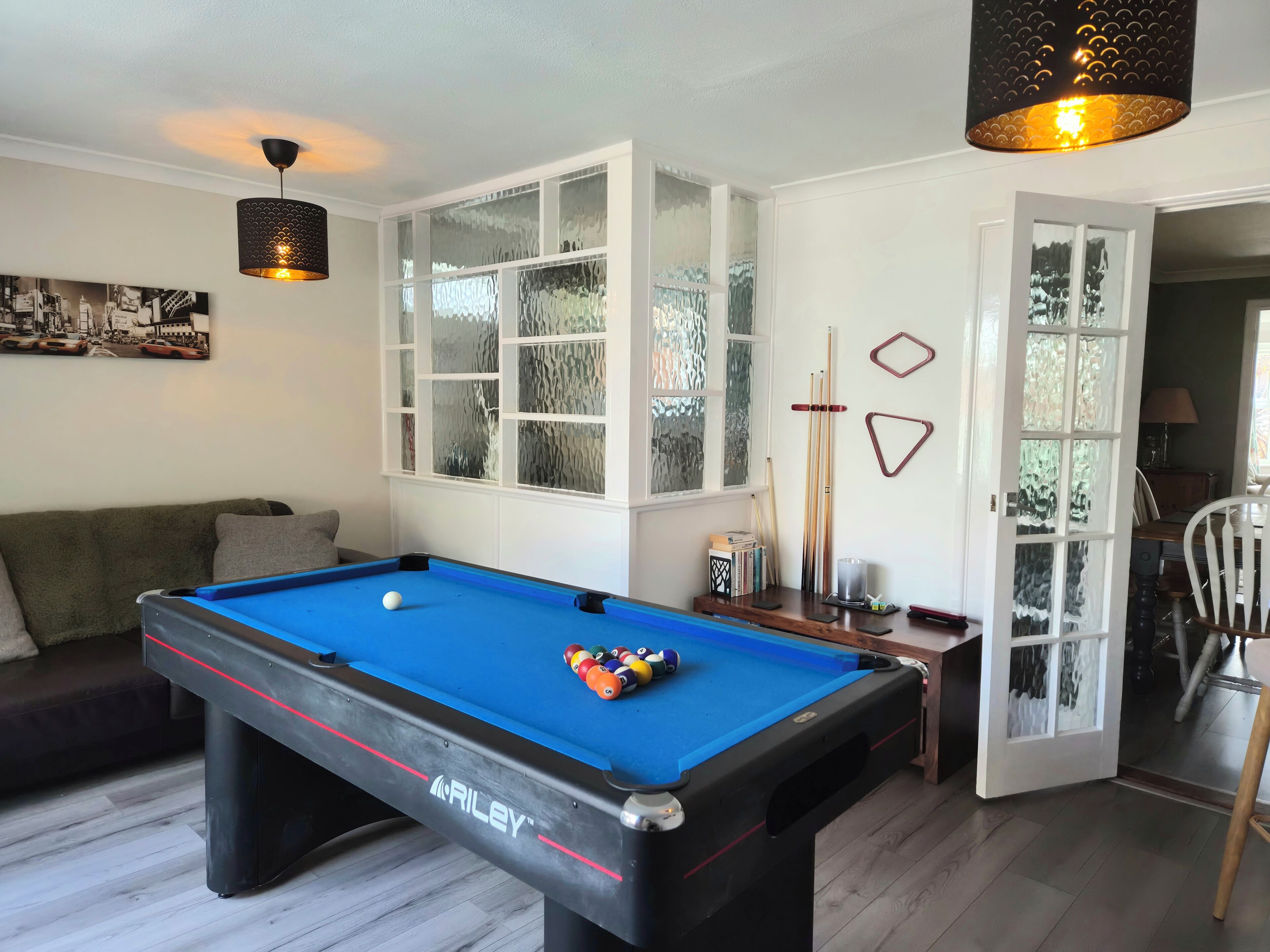 A pool table with a blue felt surface, a billiards cue rack, and a billiard ball set.