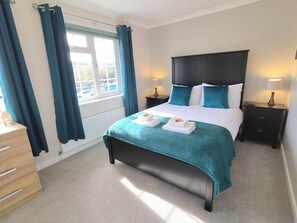 A neatly made bed with a teal bedspread, two pillows, and two bedside lamps.