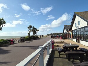 Un paseo marítimo con bancos, una cafetería y vistas al mar.