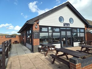 A restaurant with outdoor seating, a sign for 'Pebbles Fish & Wine Bar,' and a view of the sea.