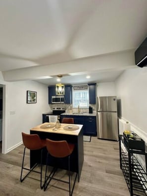 A compact kitchen with a central island, dark blue cabinets, stainless steel appliances, and a modern light fixture.