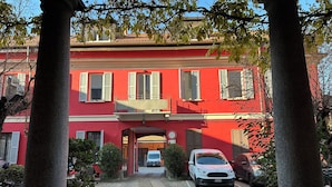 Un edificio rojo con una entrada de piedra, un coche estacionado al frente y un cielo despejado.