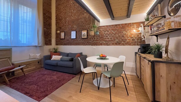 Una sala de estar acogedora con pared de ladrillo, un sofá, una mesa de comedor con sillas y una alfombra roja.
