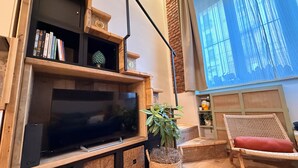 Sala de estar con televisión de pantalla plana, estanterías de madera, una planta y una pantalla de proyección que muestra una imagen de un edificio.