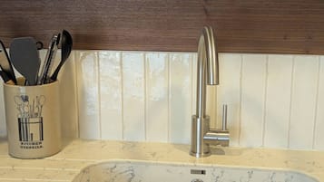 A kitchen sink with a modern faucet, a utensil holder, and a wooden shelf above.