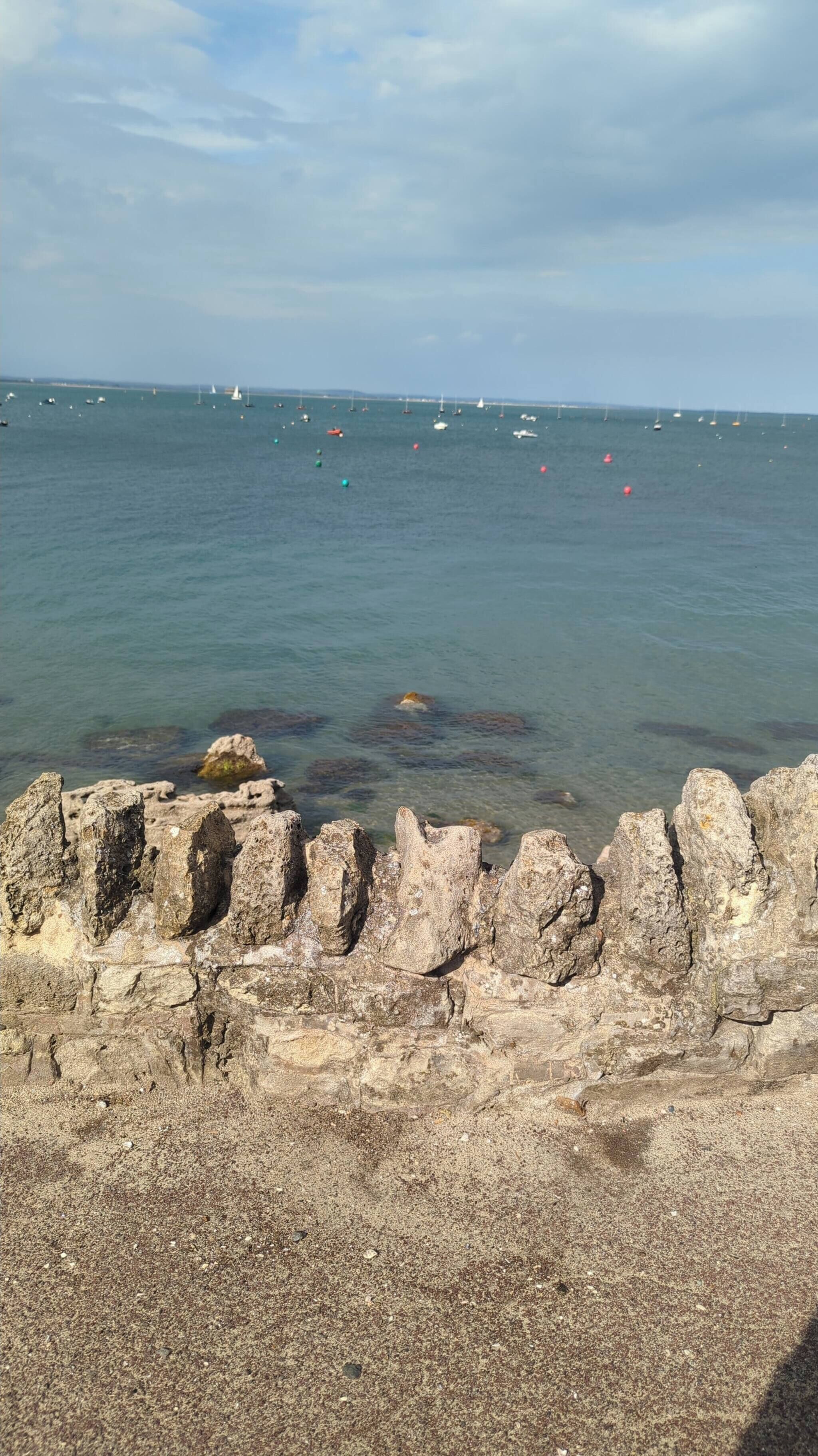 A rocky shoreline with clear water and boats in the distance.