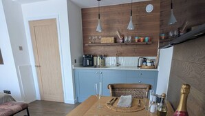 A dining area with a wooden table set for two, a bottle of wine, and a wicker chair. - Stylish New Apartment in Central Seaview - 5 Star Comfort! (Seaview)