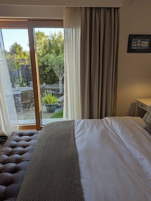 A hotel room with a large bed, a view of the outdoor garden, and a sliding glass door. - Stylish New Apartment in Central Seaview - 5 Star Comfort! (Seaview)