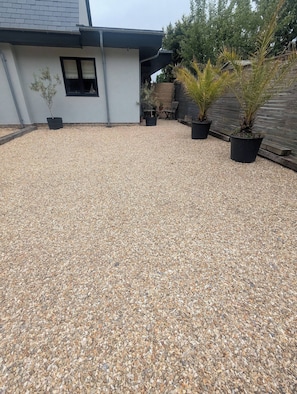 A gravel driveway leading to a house with a white exterior and a black window. There are several potted plants along the driveway. - Stylish New Apartment in Central Seaview - 5 Star Comfort! (Seaview)
