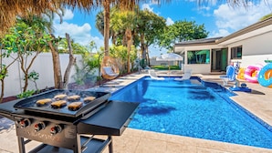 Un giardino sul retro con piscina, area barbecue e poltrona relax.