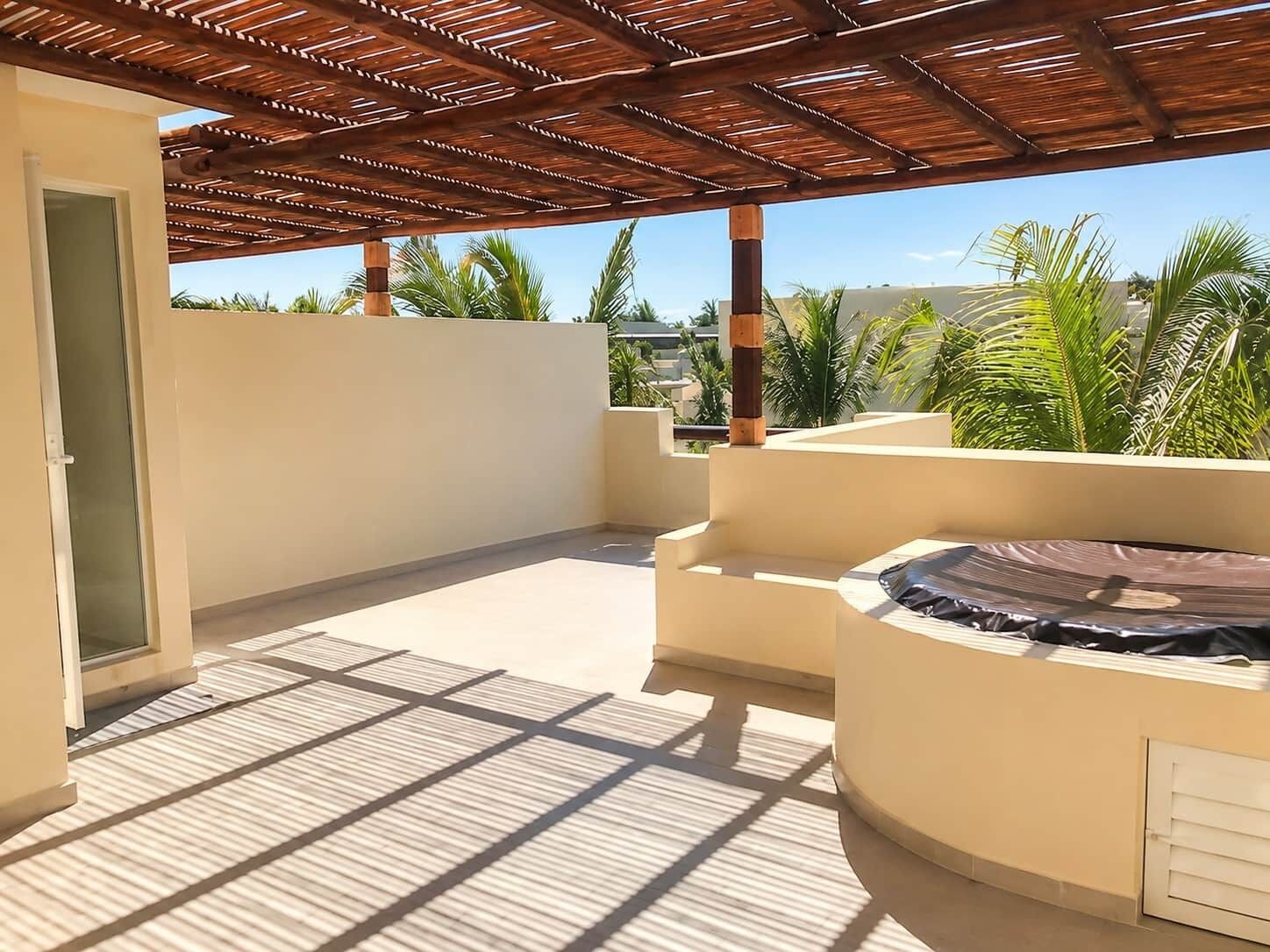 A covered outdoor area with a seating arrangement, a door, and a view of palm trees.