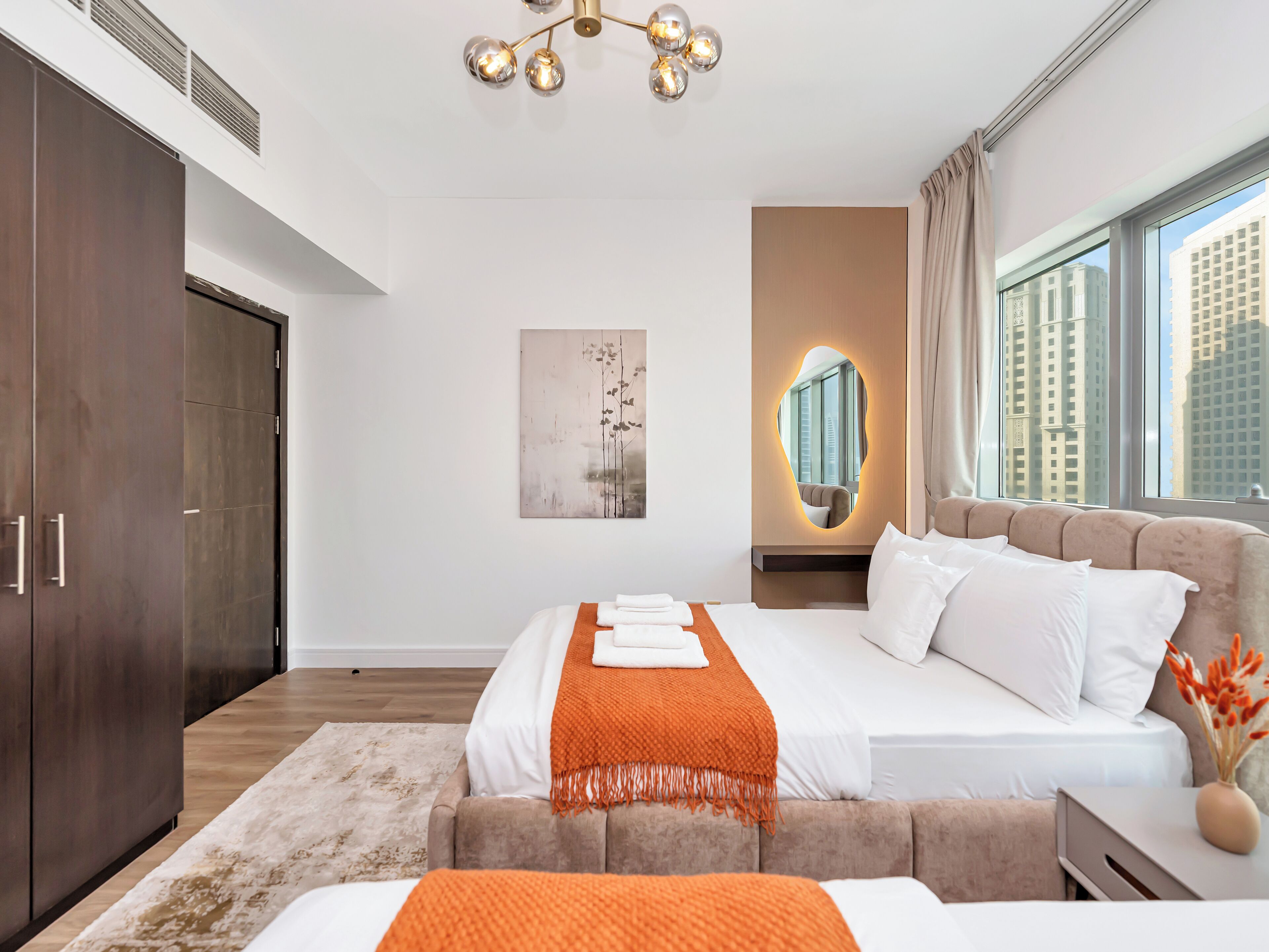 Une chambre d’hôtel moderne, dotée d’un grand lit, d’une armoire, d’un miroir et offrant une vue sur la ville.