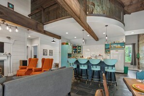 A spacious living area with a high ceiling, wooden beams, and a kitchen with a bar area. - Eclectic Lakefront Cottage on Great East Lake! (Acton)